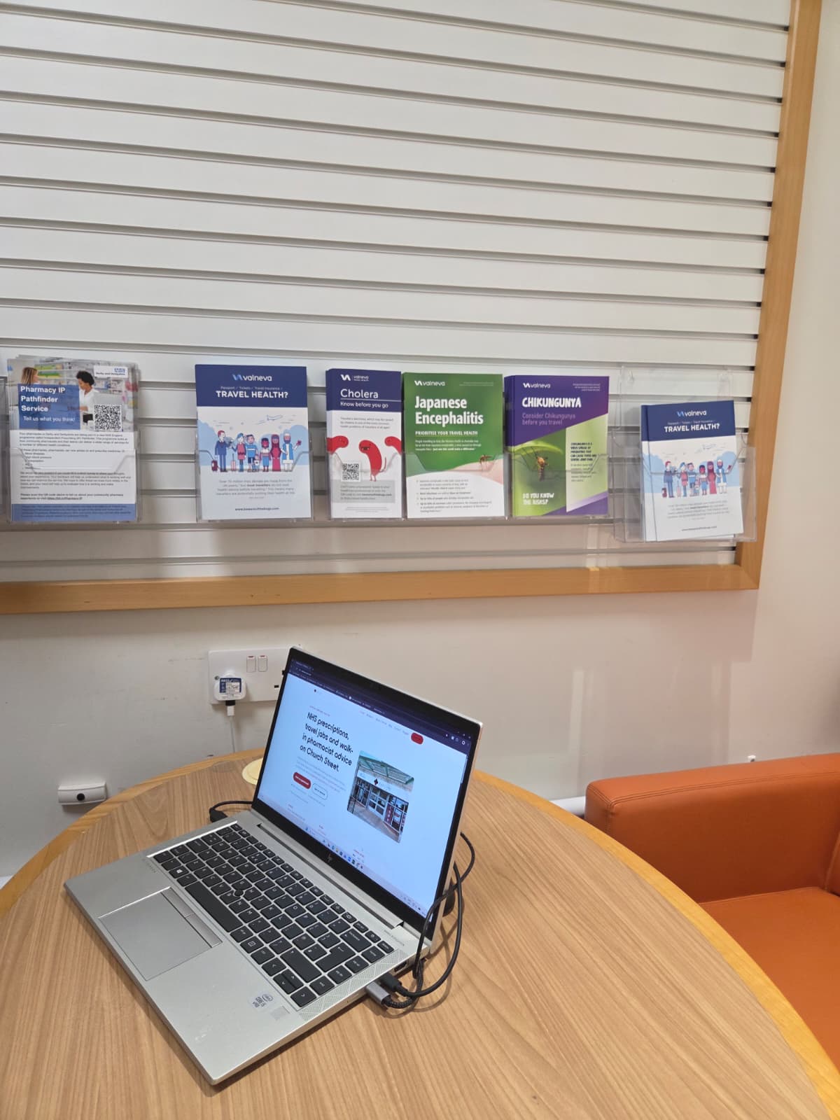 Travel vaccination leaflets and booking laptop at the Medicine Stop consultation desk, Alfreton.